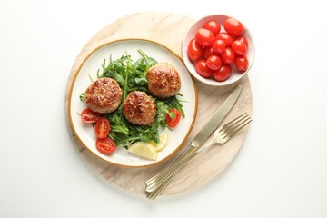 Delicious patties with greens, tomatoes and cutlery on white table, top view
