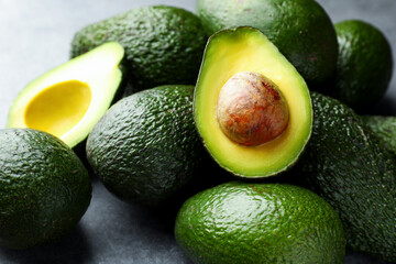 Many whole and cut avocados on light grey table, closeup
