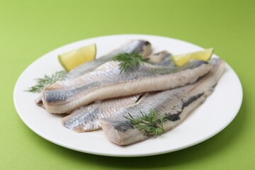 Marinated herring fillets with lime and dill on green background, closeup