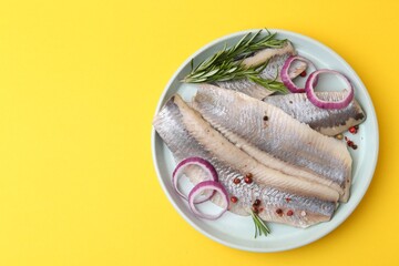 Marinated herring fillets with onion rings, rosemary and peppercorns on yellow background, top...