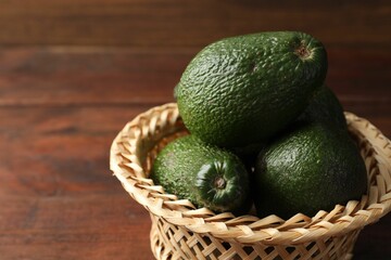 Whole avocados in wicker basket on wooden table, closeup. Space for text