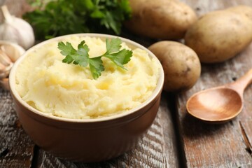 Delicious mashed potato with parsley, garlic and spoon on wooden table, closeup