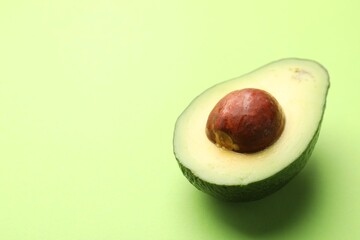 Half of fresh avocado on light green background, closeup. Space for text