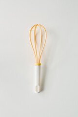 Whisk with yellow silicone strands on a clean white background in a kitchen setting