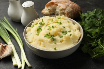 Delicious mashed potato with green onions served on black table, closeup