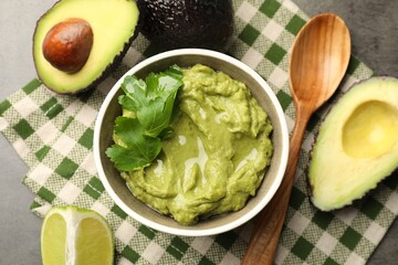 Tasty avocado dip in bowl, parsley and fruits on grey table, flat lay