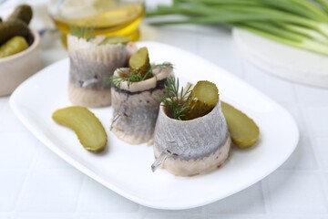 Delicious herring rolls with pickles and dill on light table, closeup