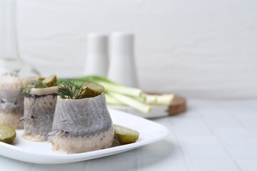 Delicious herring rolls with pickles and dill on light tiled table, closeup. Space for text
