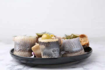 Delicious herring rolls with olives, pickles and dill on light marble table, closeup