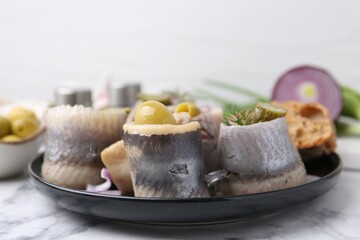 Delicious herring rolls with olives, pickles, dill and onion on light marble table, closeup