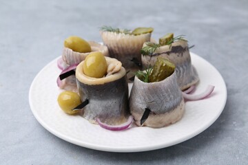 Delicious herring rolls with olives, pickles, dill and onion on gray table, closeup