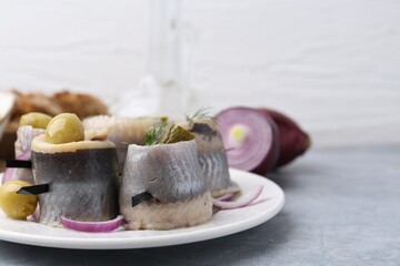 Delicious herring rolls with olives, pickles, dill and onion on gray table, closeup. Space for text