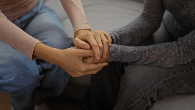 Women holding hands in support sitting indoors, expressing love and family bond in a cozy home environment with a focus on sisterhood and togetherness.