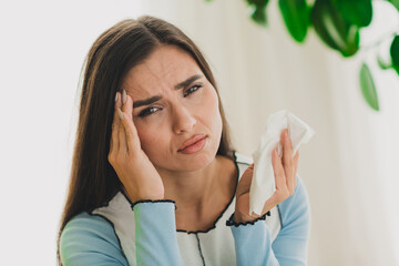 Young woman experiencing discomfort while holding a tissue indoors, expressing emotions in a bright...