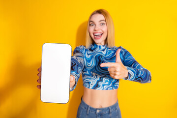 Young woman showing smartphone on vibrant yellow background promoting digital content