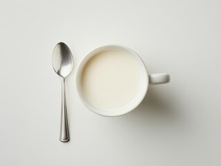White mug of milk with spoon on white surface