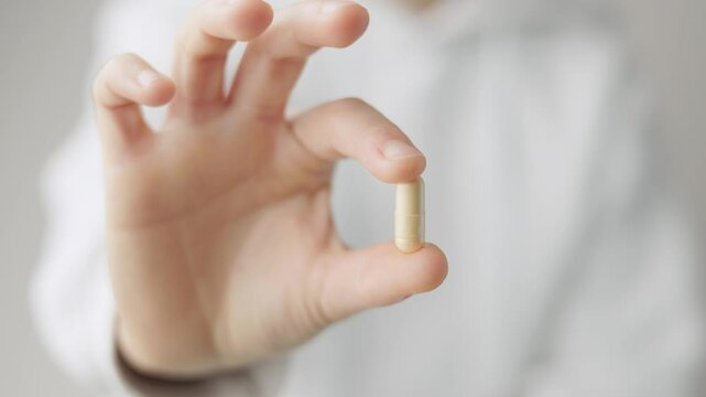 A woman shows a q10 coenzyme capsule pill, with her right hand to the camera, she wears a white sweatshirt on white background