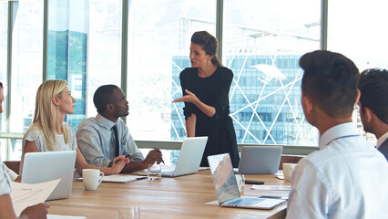 Businesswoman Giving Presentation To Business Team Sitting Around Table In Modern Office