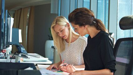 Two Female Business Colleagues Sitting At Desk In Office Discussing Documents