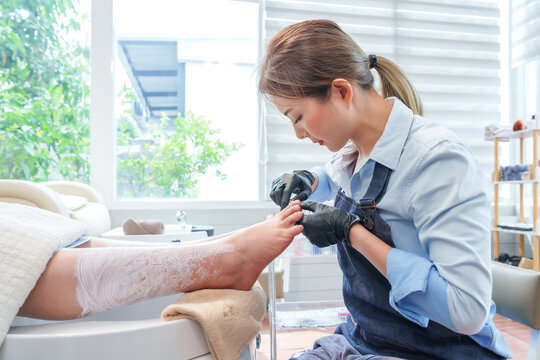 Asian female nail spa specialist trimming client's toenails with precision clippers during a luxury pedicure session. Professional foot care enhancing hygiene, beauty, and relaxation in a modern salon