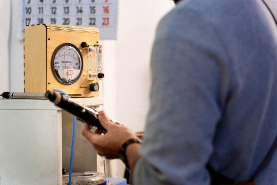 Technician repairing clarinet using manometer in workshop