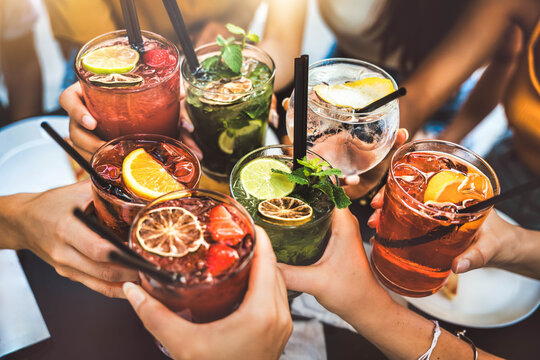 Happy people toasting cocktail glasses sitting at bar table - Cheerful friends enjoying happy hour at pub restaurant balcony - Food and beverage life style concept