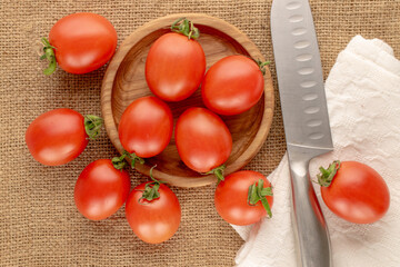 Juicy cocktail tomatoes with a wooden plate and knife, on a jute cloth, close-up, top view.