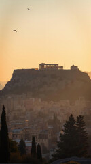Fototapeta premium Sunrise Acropolis of Athens, Greece: Aerial View with Golden Hour Glow on Ancient Marble Columns, Dreamlike Morning Fog, Overlay of Sunset Photo.