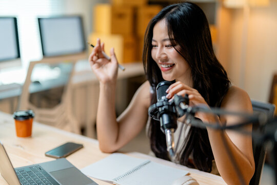 Asian woman vlogger recording podcast using microphone and laptop at her home studio