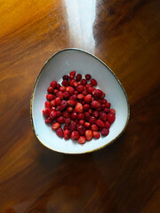 Wild strawberries in a plate on a polished wooden table. Fragaria vesca berry. Close-up,...