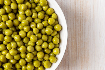 Bowl of canned green peas over white wooden tabletop. Wet marinated sweet peas as snack and salad ingredient. Vegetarian food, vegetable protein and dietary fiber.