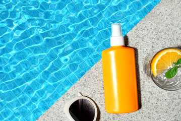 Sunscreen lotion and cocktail drink near pool water