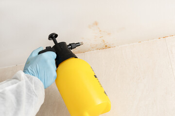 Close up of a person cleaning mold in a bathroom with a sprayer wearing a protective suit