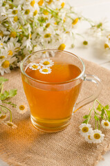 Chamomile tea in a transparent cup on a white wooden background with a bouquet of daisies with selective focus