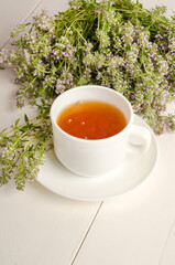Herbal tea with thyme in a white cup on a white wooden background with a bouquet of blooming herbs with selective focus