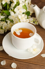 A cup of fragrant jasmine tea with fresh jasmine flowers on a dark wooden background