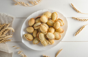Delicious cookies in the shape of a nut filled with boiled condensed milk on a white wooden background, flat lay