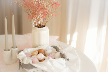 A light Easter composition with colorful Easter eggs in a basket, natural fabric, and dried...