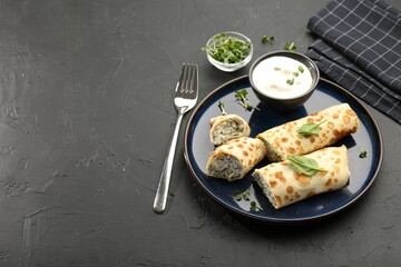 Delicious crepes with cottage cheese, spinach and sour cream served on black table. Space for text