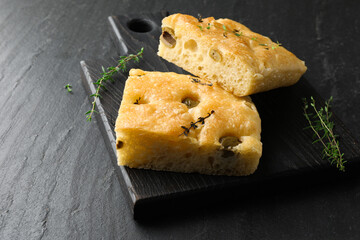 Pieces of delicious focaccia bread with olives and thyme on black table, closeup. Space for text