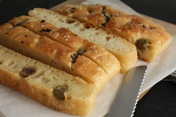 Slices of delicious focaccia bread with olives, thyme, salt and knife on black table, closeup