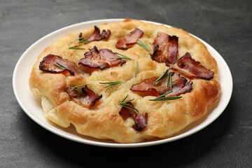 Delicious focaccia bread with bacon and rosemary on black table, closeup