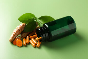 Turmeric capsules, roots and overturned medical bottle on green background