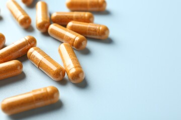 Turmeric capsules on light blue background, closeup. Space for text