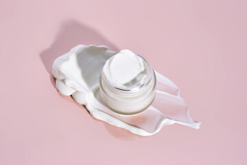 An open jar of cream with its texture on a pink background.