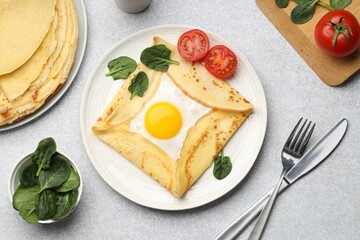 Delicious crepes with egg, tomatoes and basil on light grey table, flat lay
