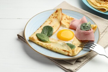 Delicious crepe with egg, ham and basil on white wooden table, closeup