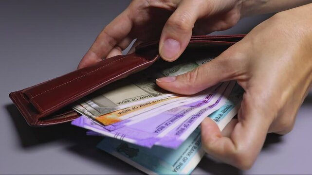 Close-up view of female hands holding wallet full of Indian cash money, counting colorful Indian rupee notes (INR) in the brown leather wallet. Wealth and success,  financial profit and security.