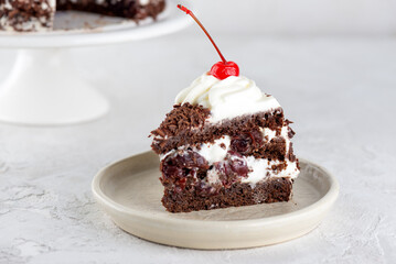 Piece of brownie cake, Black forest or Schwarzwald dessert with chocolate biscuit , cream and cherries on a white table. Vegan dessert.