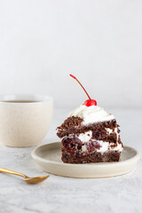 Piece of Black forest cake with cherry, cream with shea butter, cognac and chocolate biscuit and cup of coffee on a table. Vegan dessert. Vertical orientation.